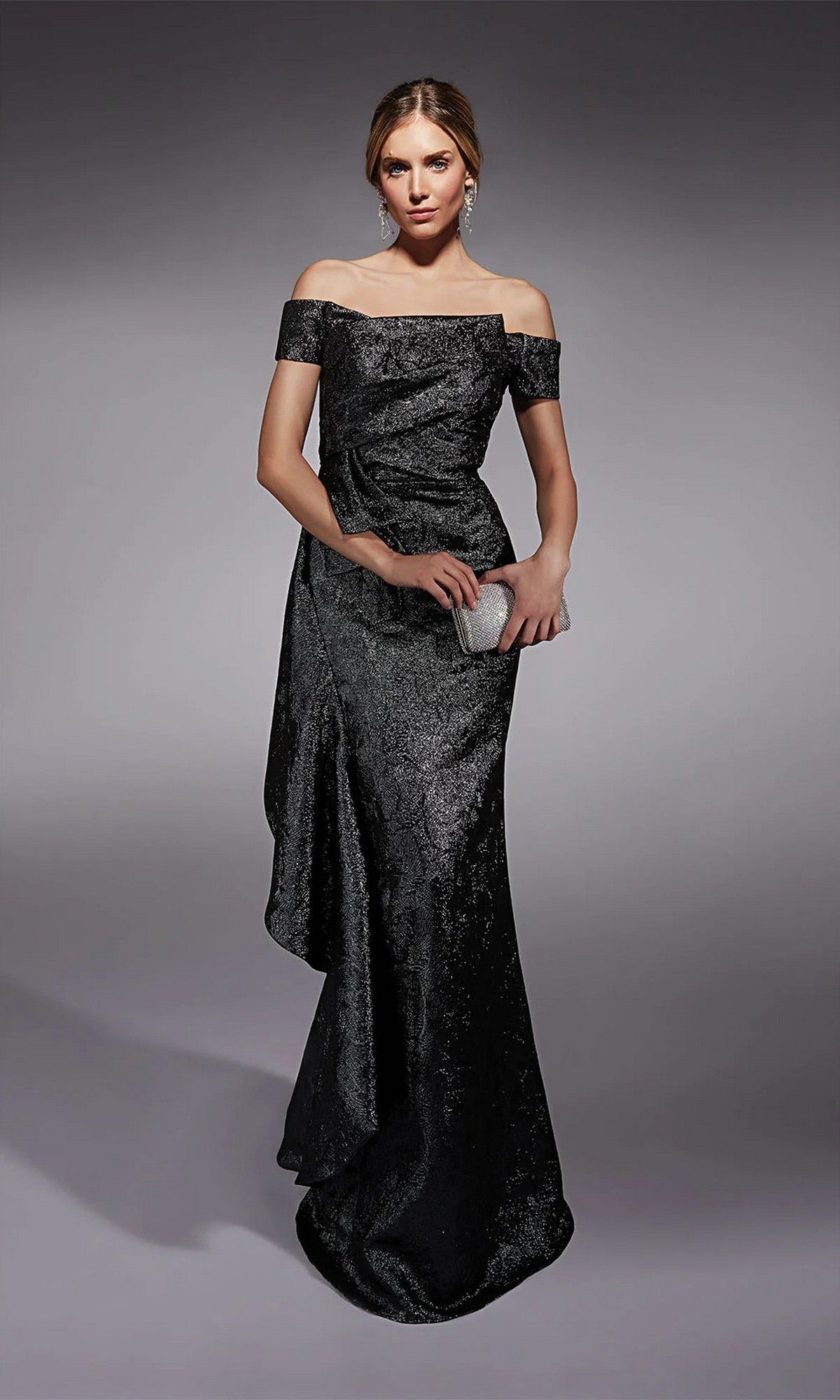 A woman in the Alyce 27735 long formal dress, off-the-shoulder and floor-length, holds a small silver clutch while standing against a plain gray background.